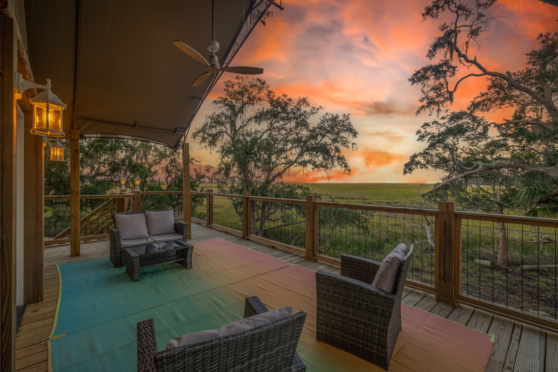 Outdoor patio with furniture, overlooking a field at sunset, colorful sky, wood railing, and tent structure.