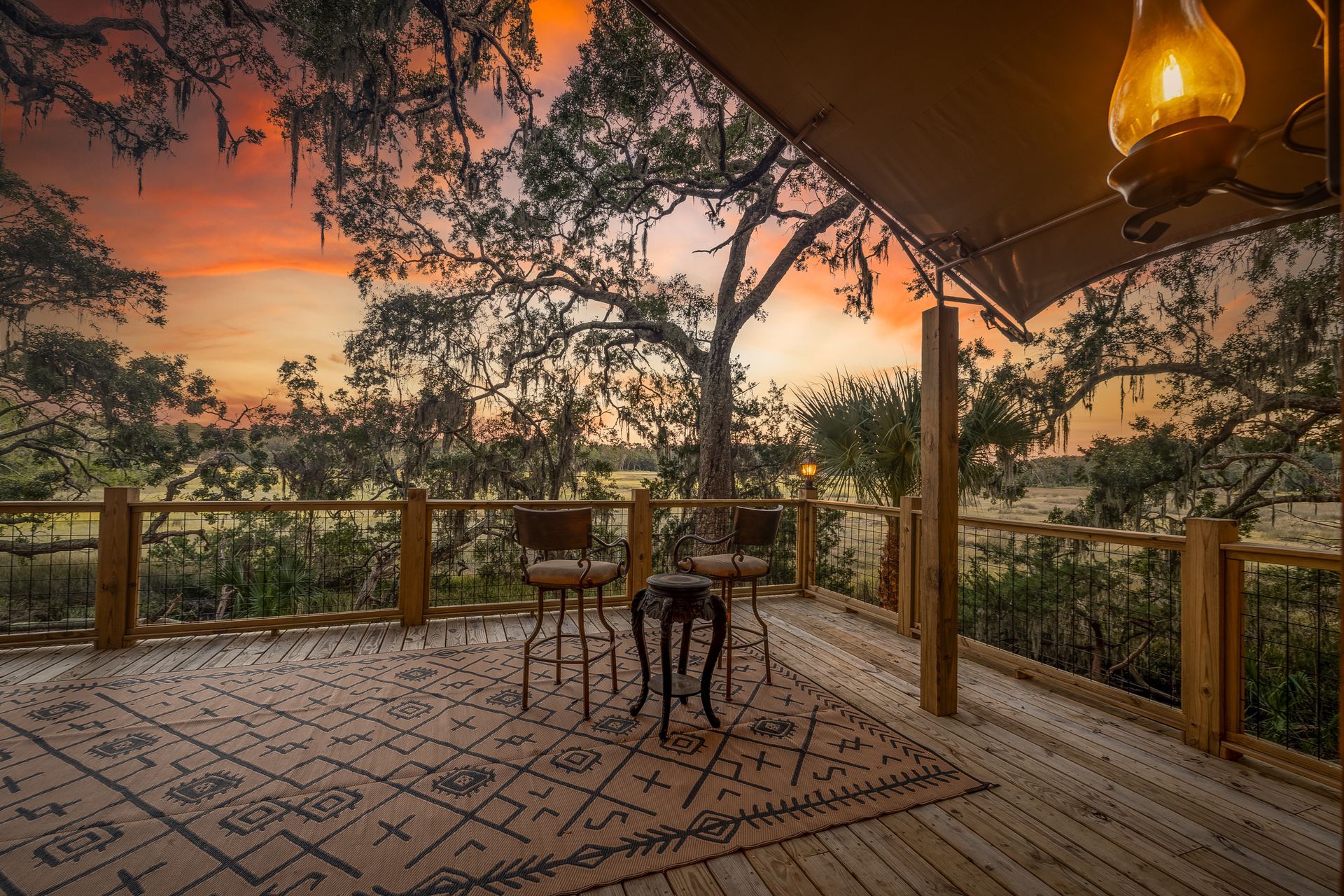 Deck overlooking a landscape, with seating and a rug; sunset colors and a lantern.
