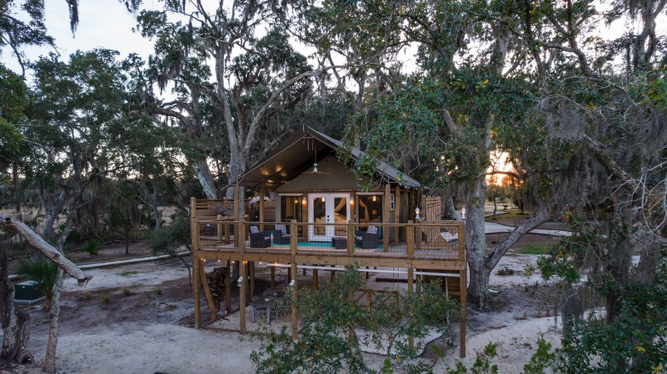 Wooden cabin on stilts surrounded by trees; dusk setting.