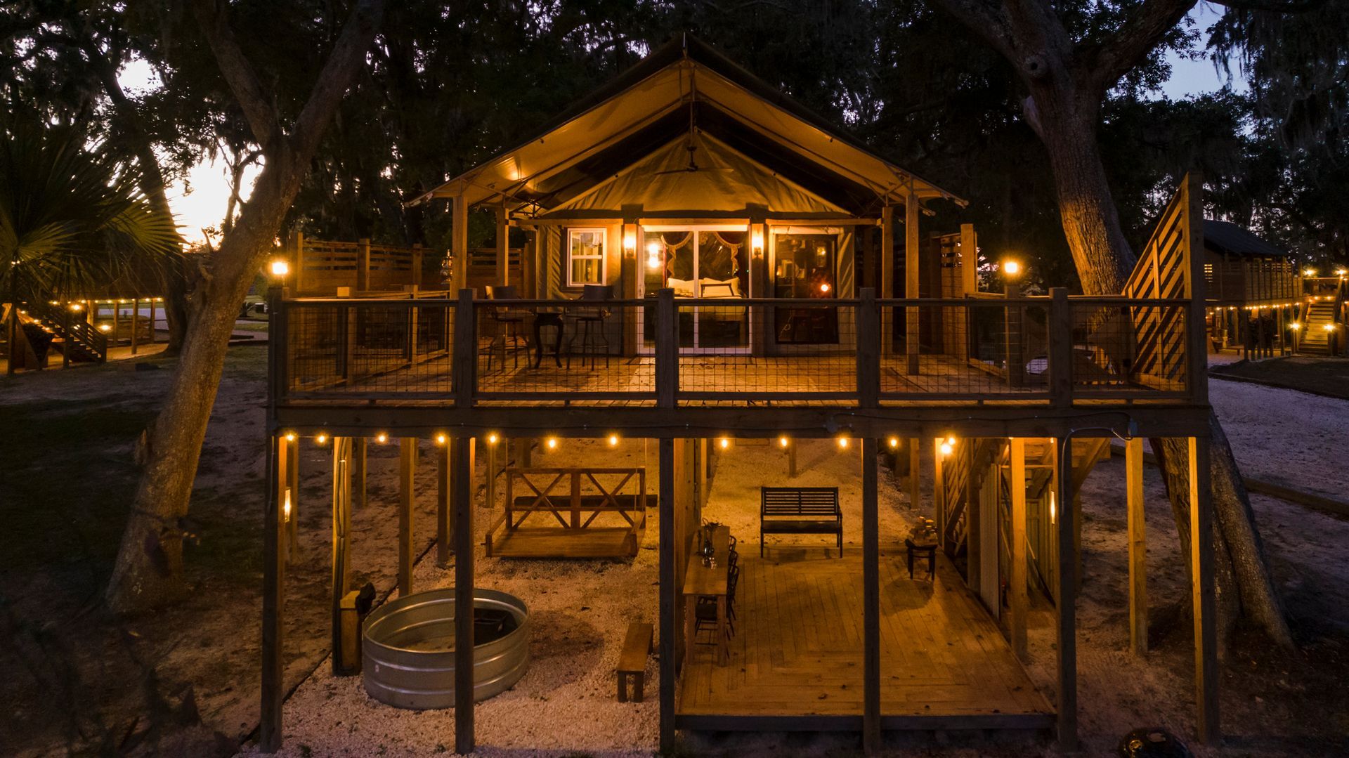 Wooden cabin with illuminated porch, string lights, and fire pit at night.