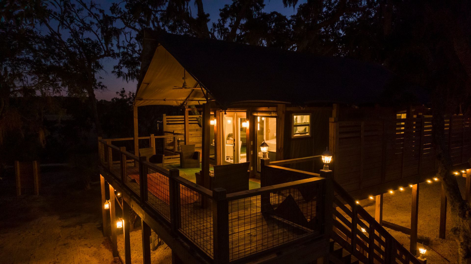 Cabin illuminated at dusk with a wooden deck, string lights, and open door.