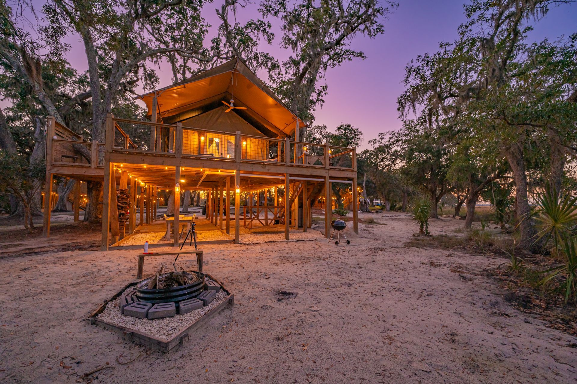 Wooden cabin on stilts surrounded by trees; dusk setting.