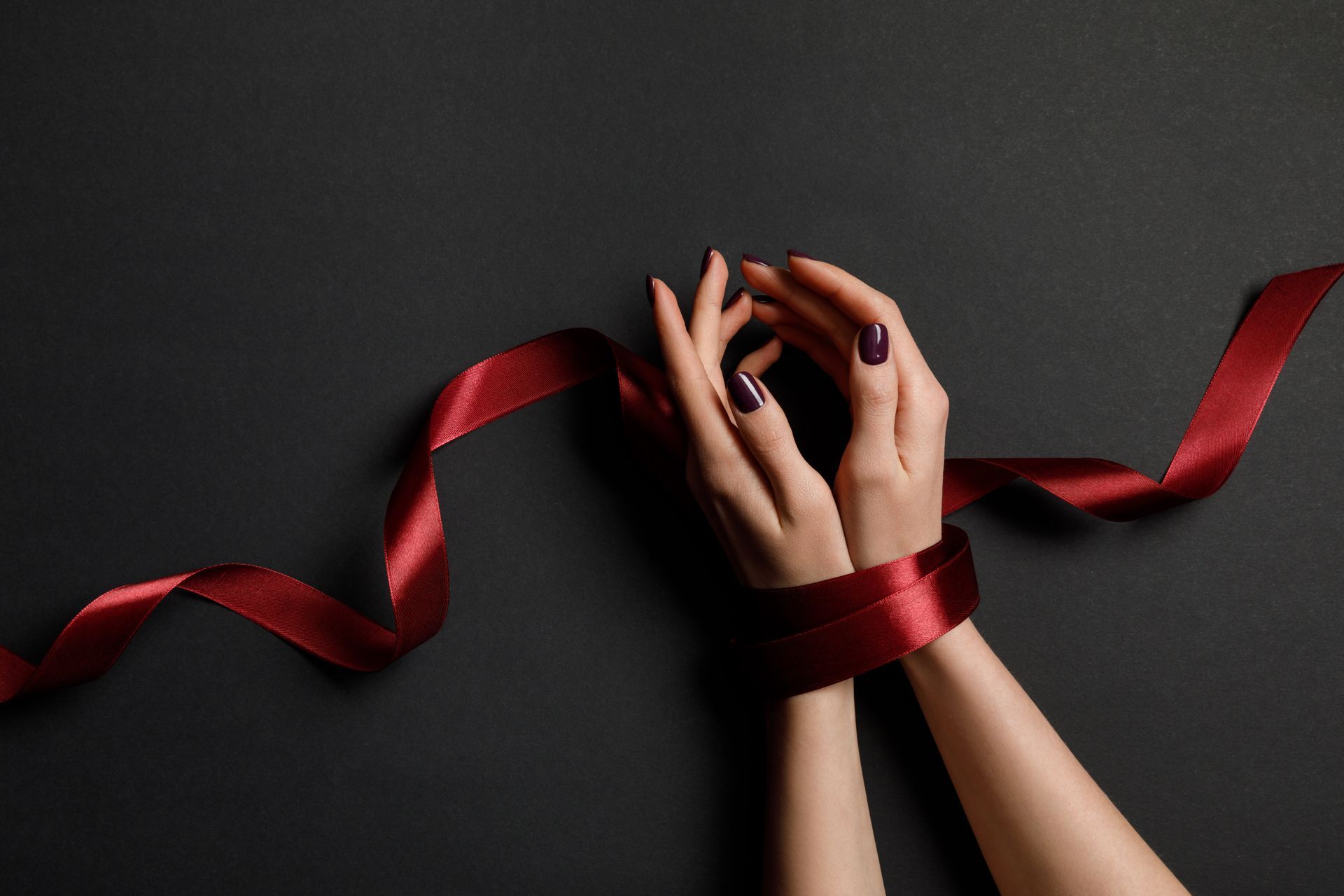 A woman 's hands are tied with a red ribbon on a black background.
