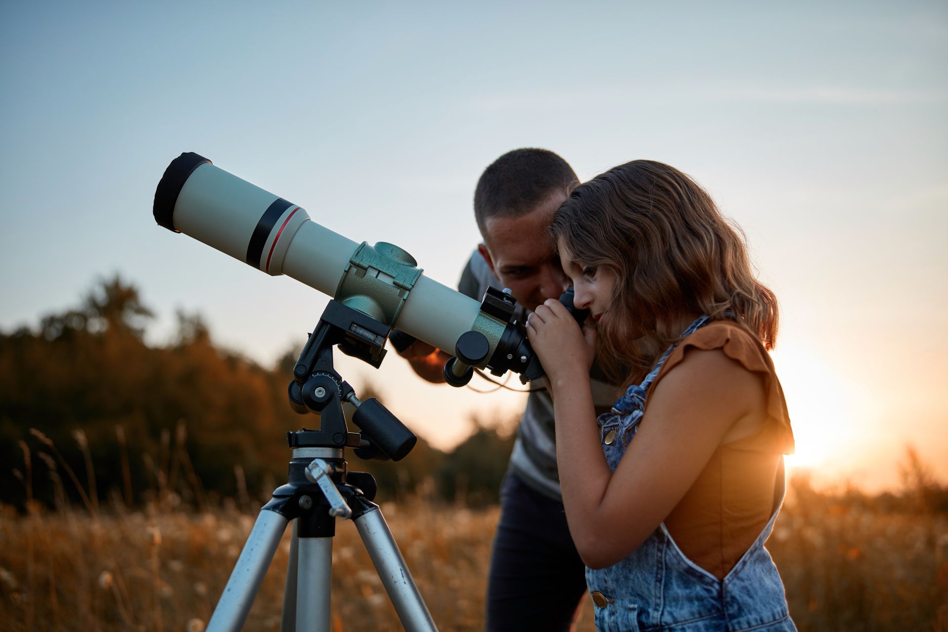 A man and a woman are looking through a telescope in a field.
