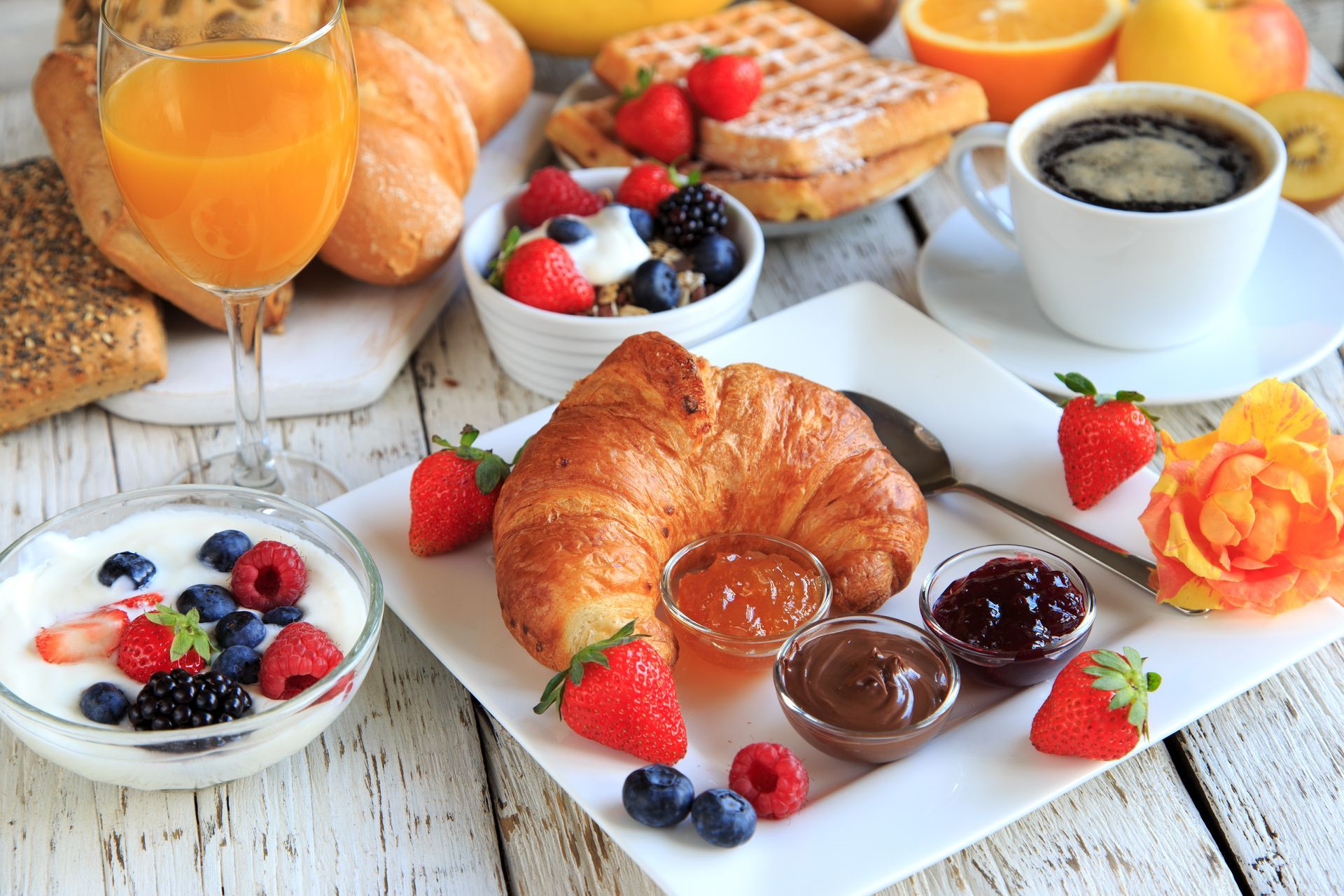A table topped with a variety of food including a croissant , jam , yogurt , fruit and coffee.