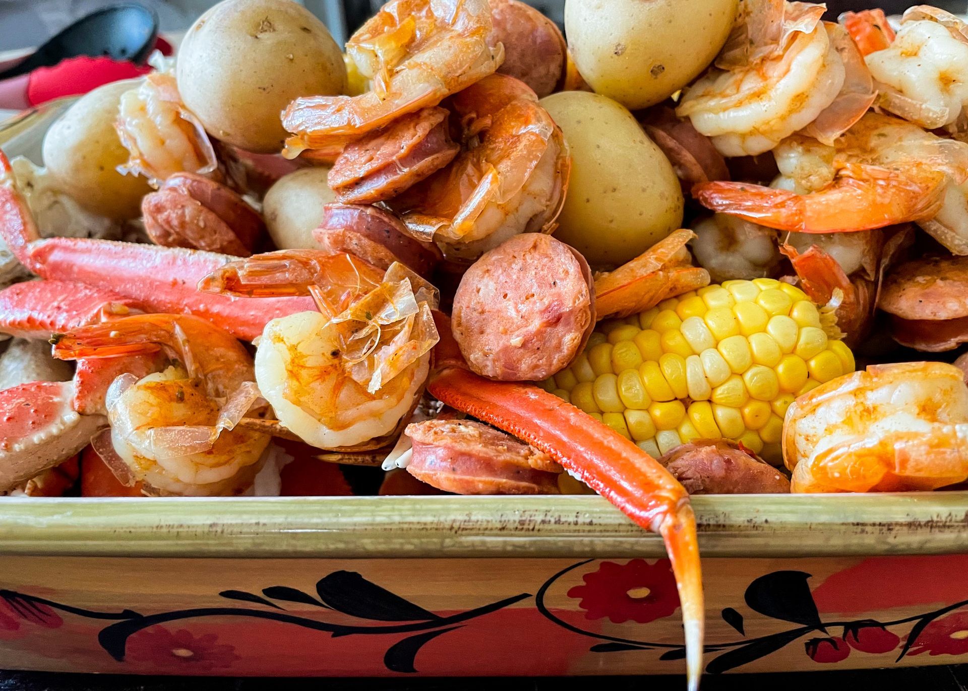 A bowl filled with shrimp , potatoes , corn and sausage.