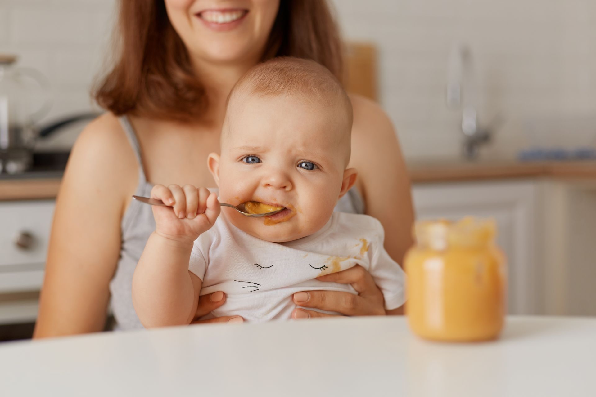 A woman is holding a baby who is eating food with a spoon.