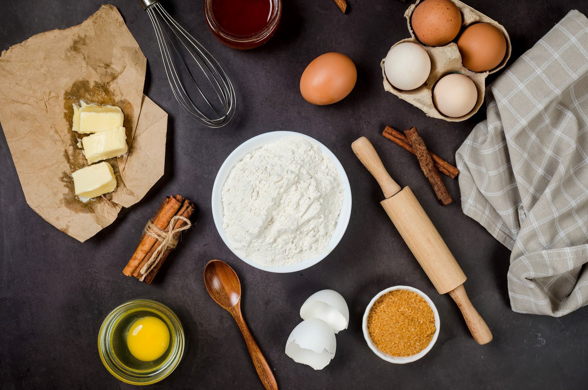 Ingredients for baking are laid out on a table including eggs , flour , butter and cinnamon sticks.