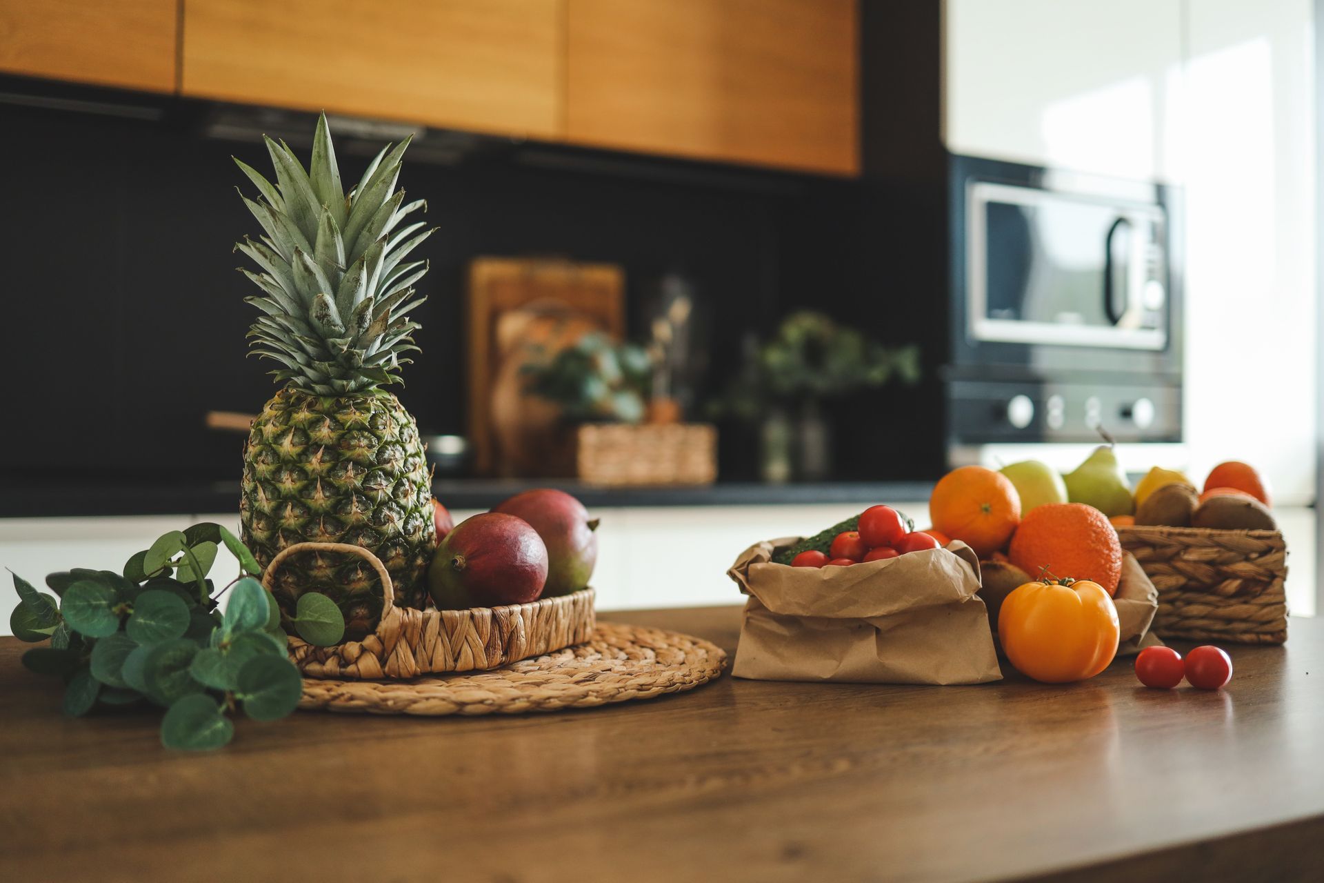 A pineapple is sitting on a wooden table next to a basket of fruit.