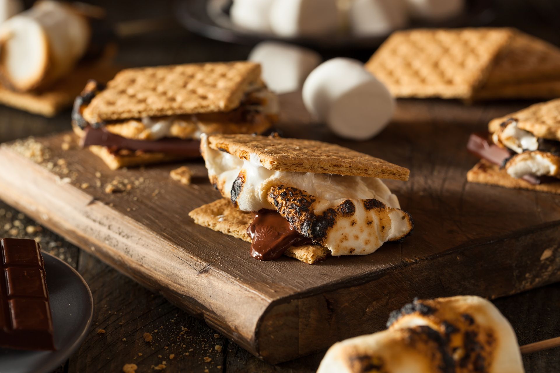 A wooden cutting board topped with s'mores and marshmallows.