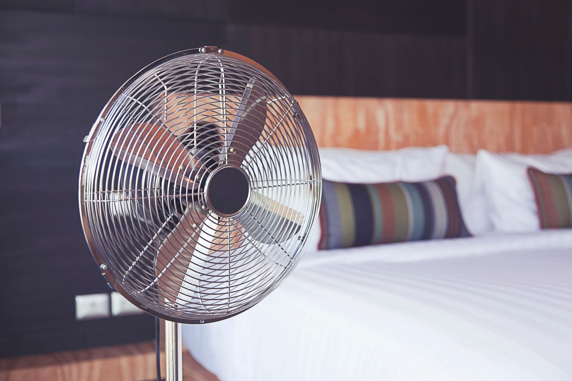 A fan is sitting in front of a bed in a bedroom.
