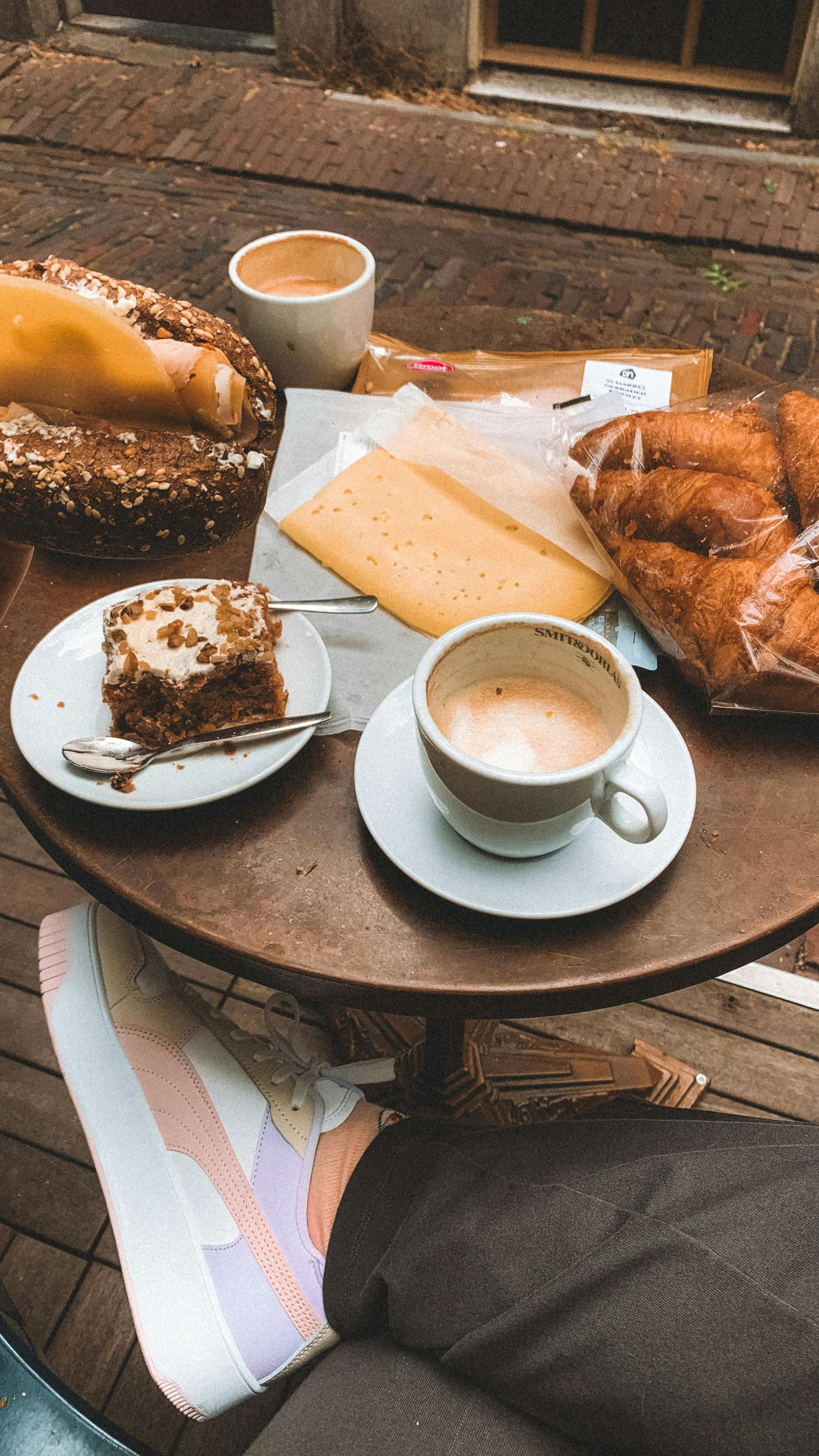 Overhead view of a cafe table with coffee, pastries, cheese, and a piece of cake.