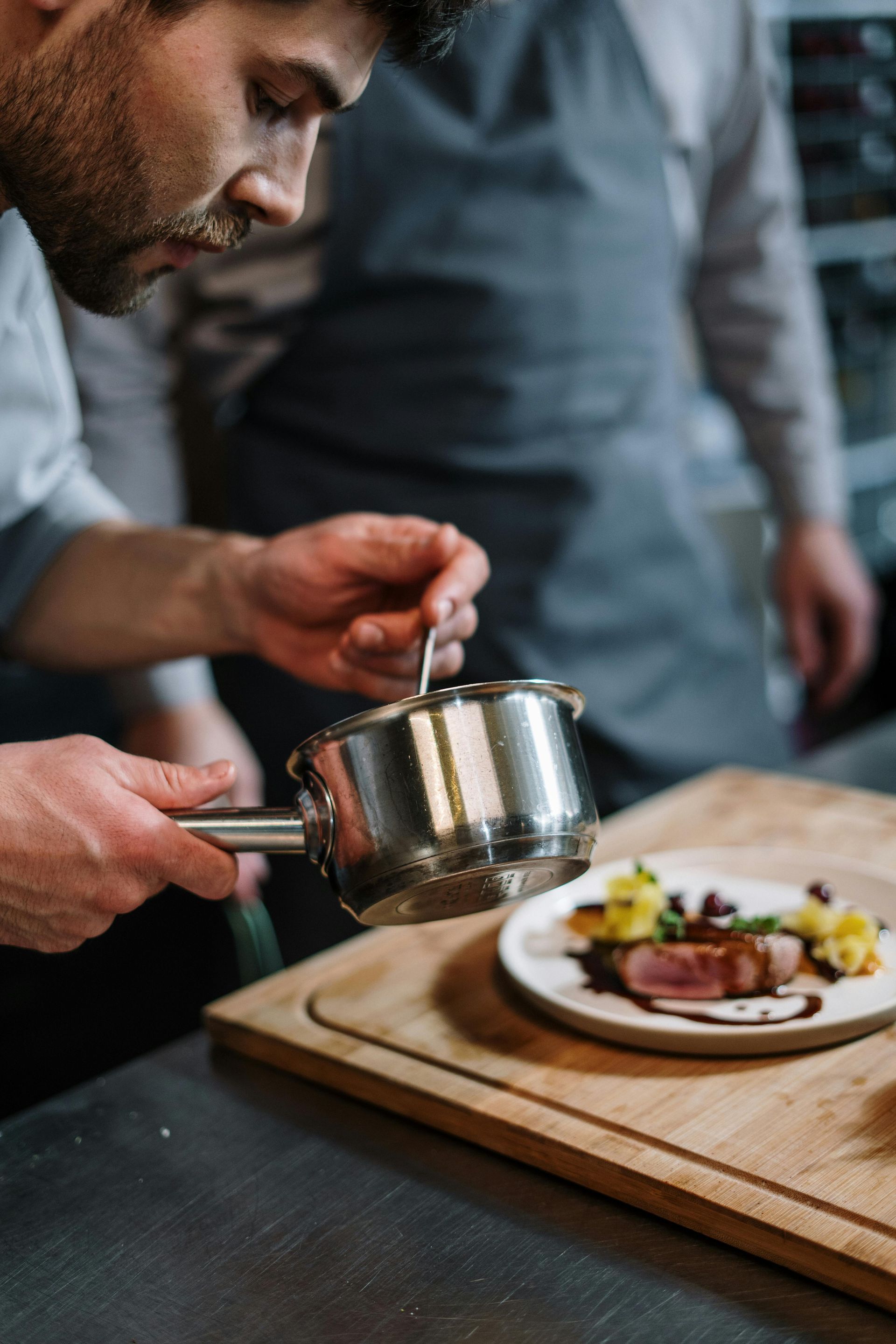Chef pouring sauce over plated dish in professional kitchen.