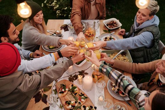 People toasting drinks around a dinner table outdoors, lit by string lights.
