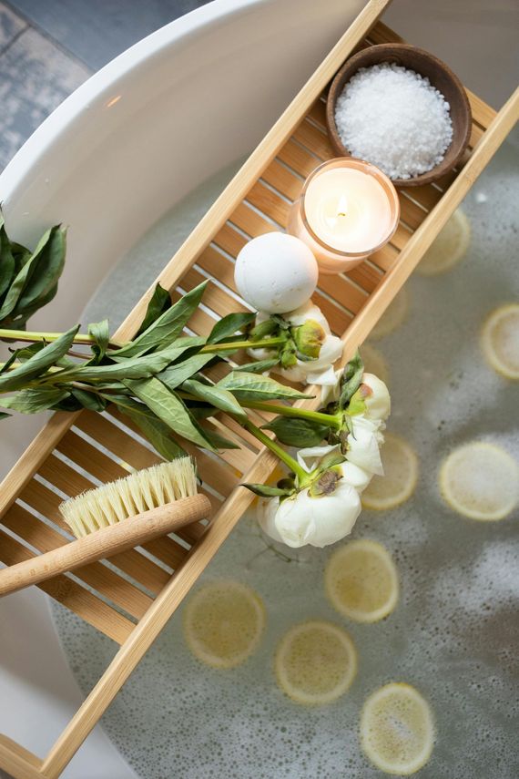Bathtub with floating lemon slices, bath salts, candles, and a flower arrangement on a bamboo caddy.