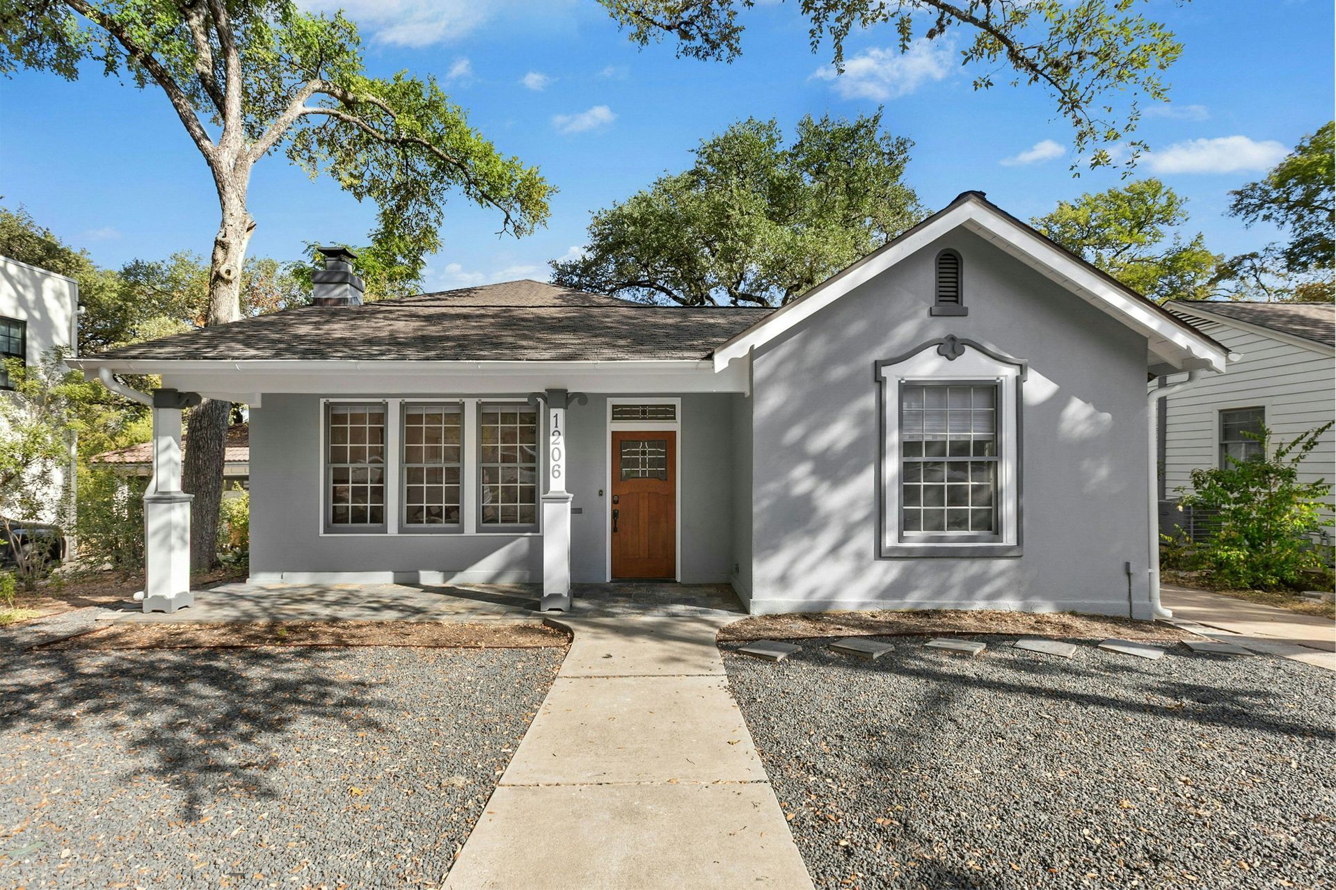 Gray house with brown door, windows, and gravel yard; sunny day.