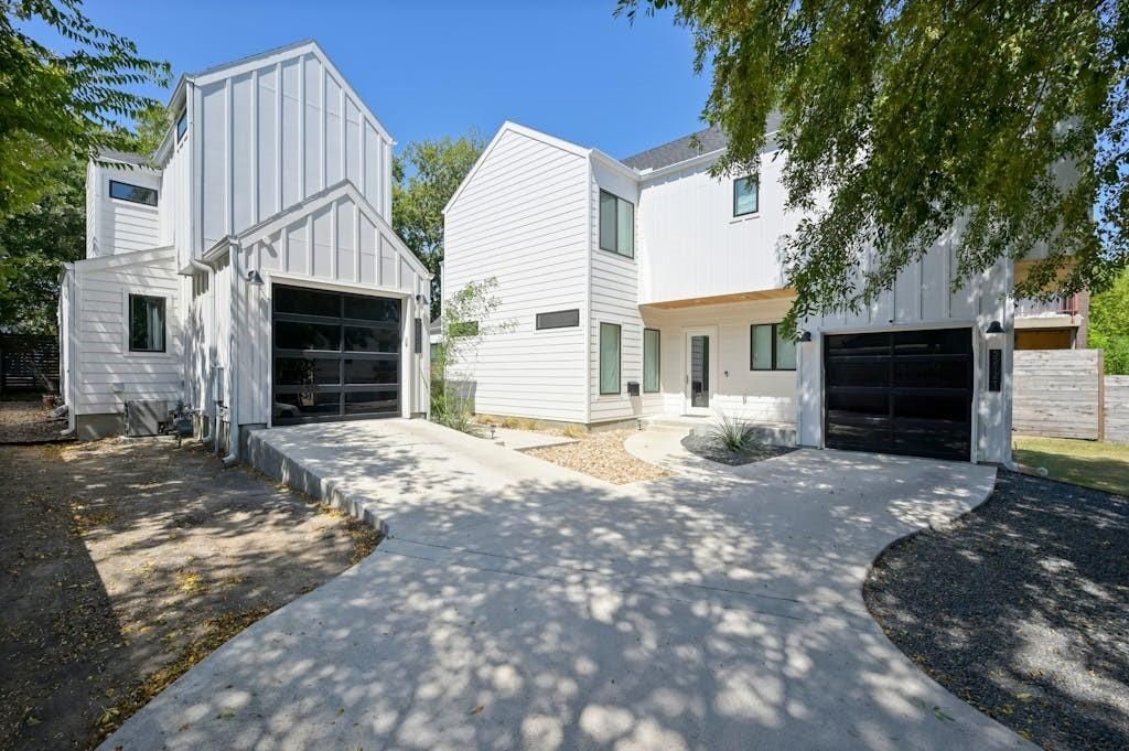 White modern home with two garages and a paved driveway.
