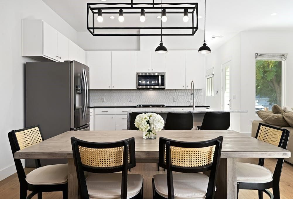 Modern kitchen and dining area with white cabinets, a black refrigerator, and a wooden table with chairs.