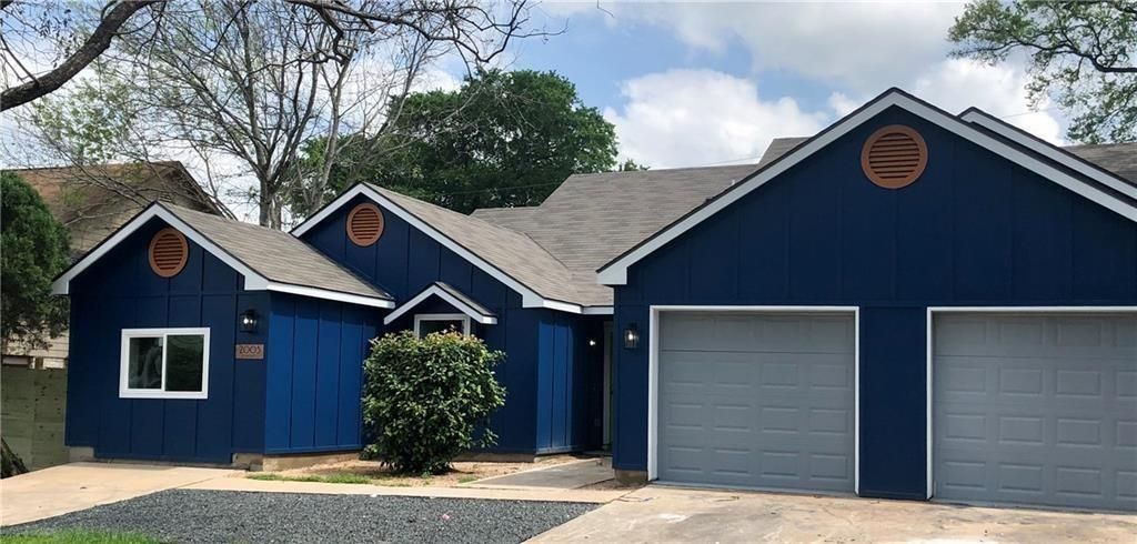 A blue house with a gray roof and two-car garage. A small tree in front and a clear sky above.