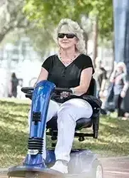 A woman is riding a blue mobility scooter in a park.