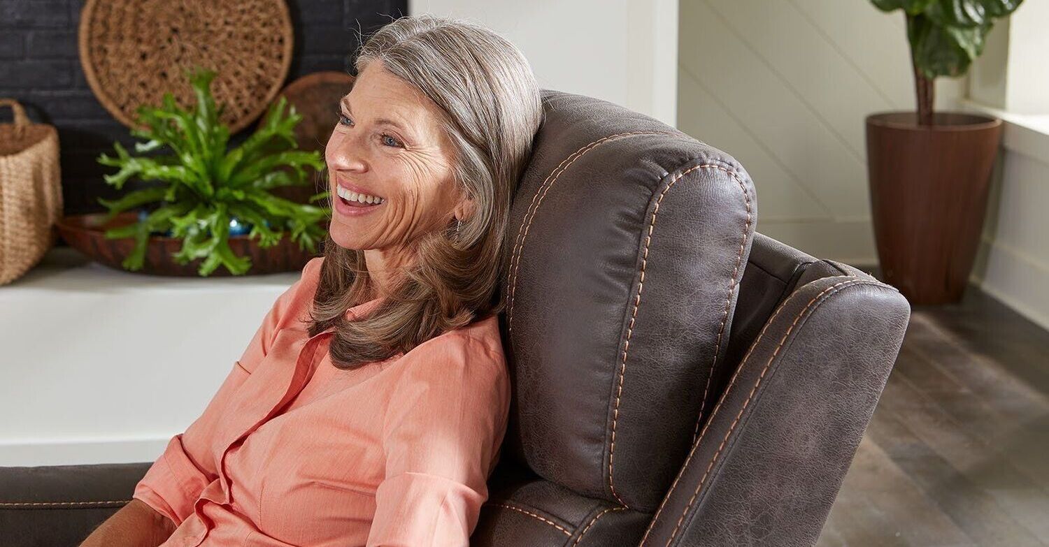 An elderly woman is sitting in a recliner in a living room.