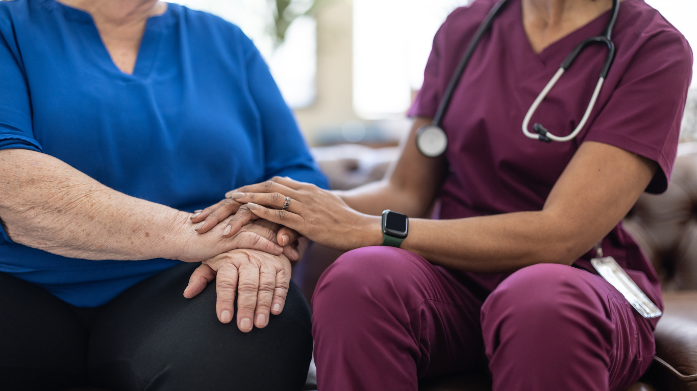 A nurse is holding the hand of an elderly woman.