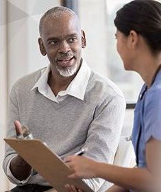 A man is talking to a nurse while holding a clipboard.