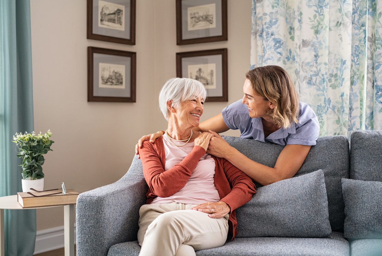 An elderly woman is sitting on a couch with a nurse.
