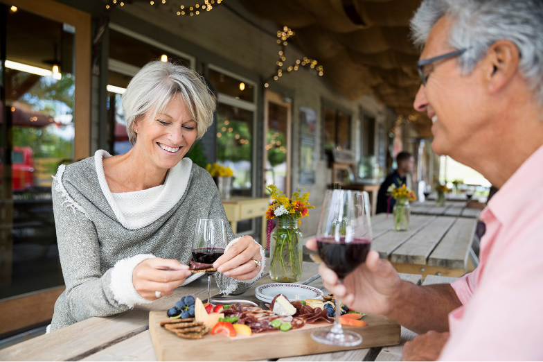 A man and a woman are sitting at a table eating food and drinking wine.