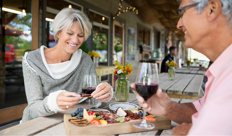 A man and a woman are sitting at a table eating and drinking wine.