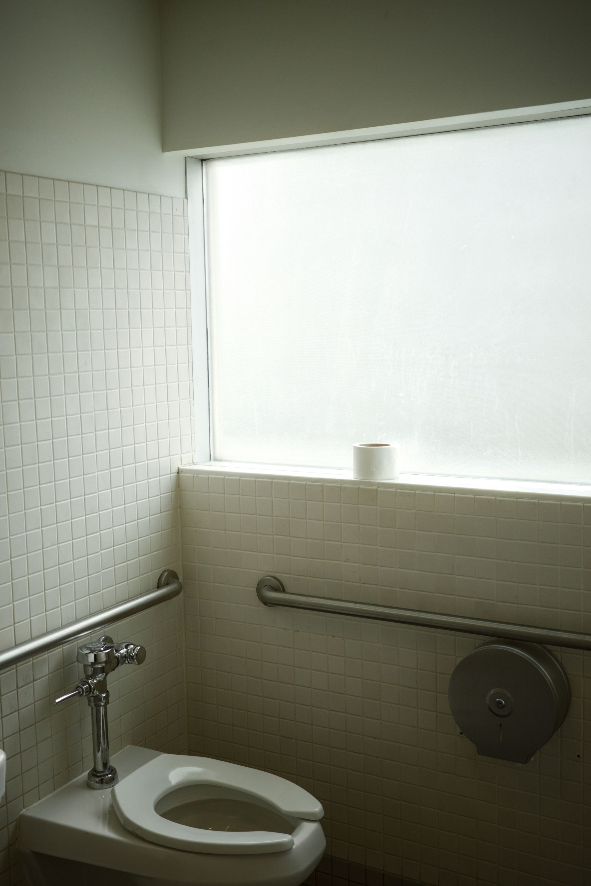 A bathroom with a toilet and a window with a roll of toilet paper on the window sill.