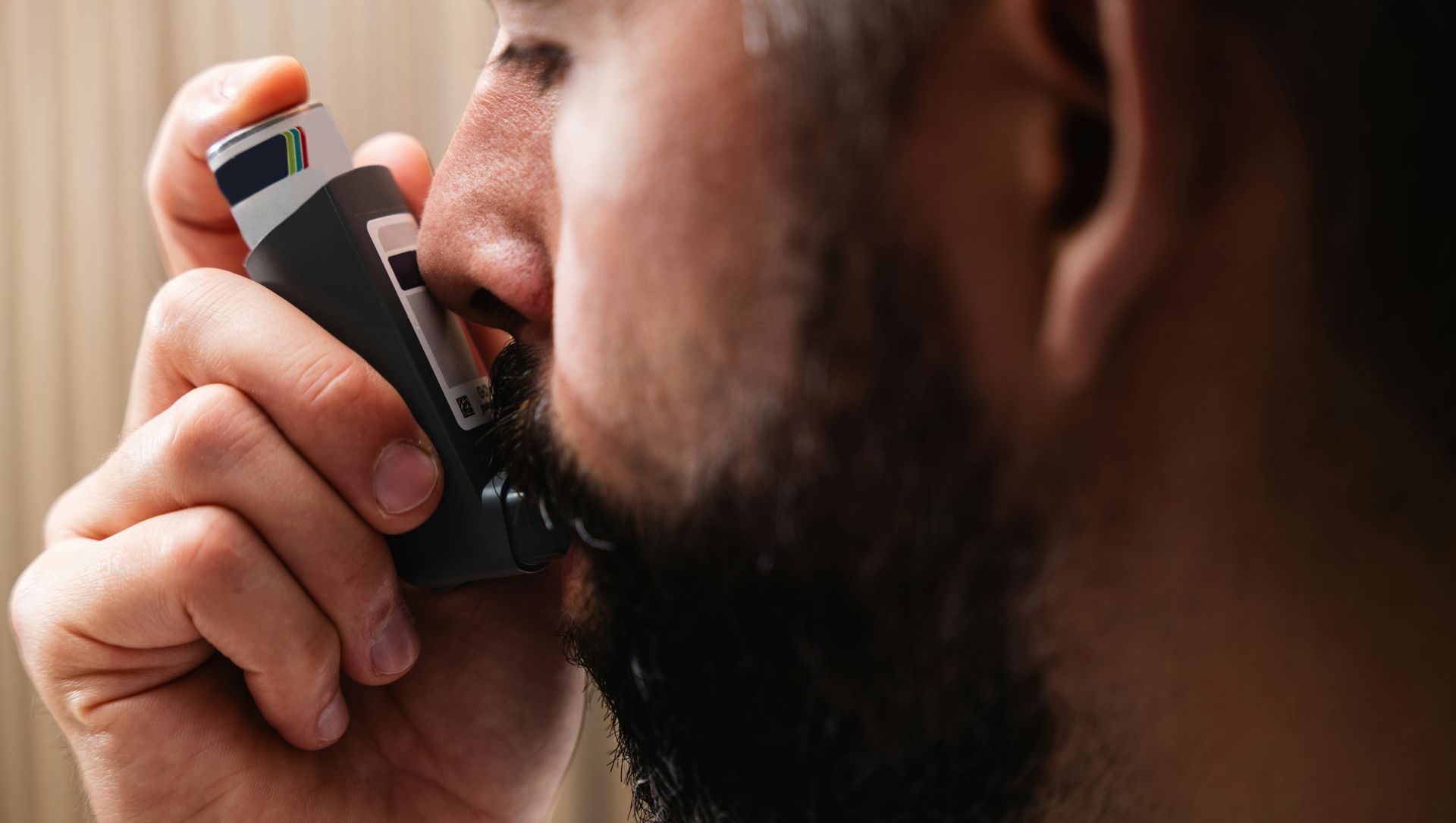 A man with a beard is using an asthma inhaler.