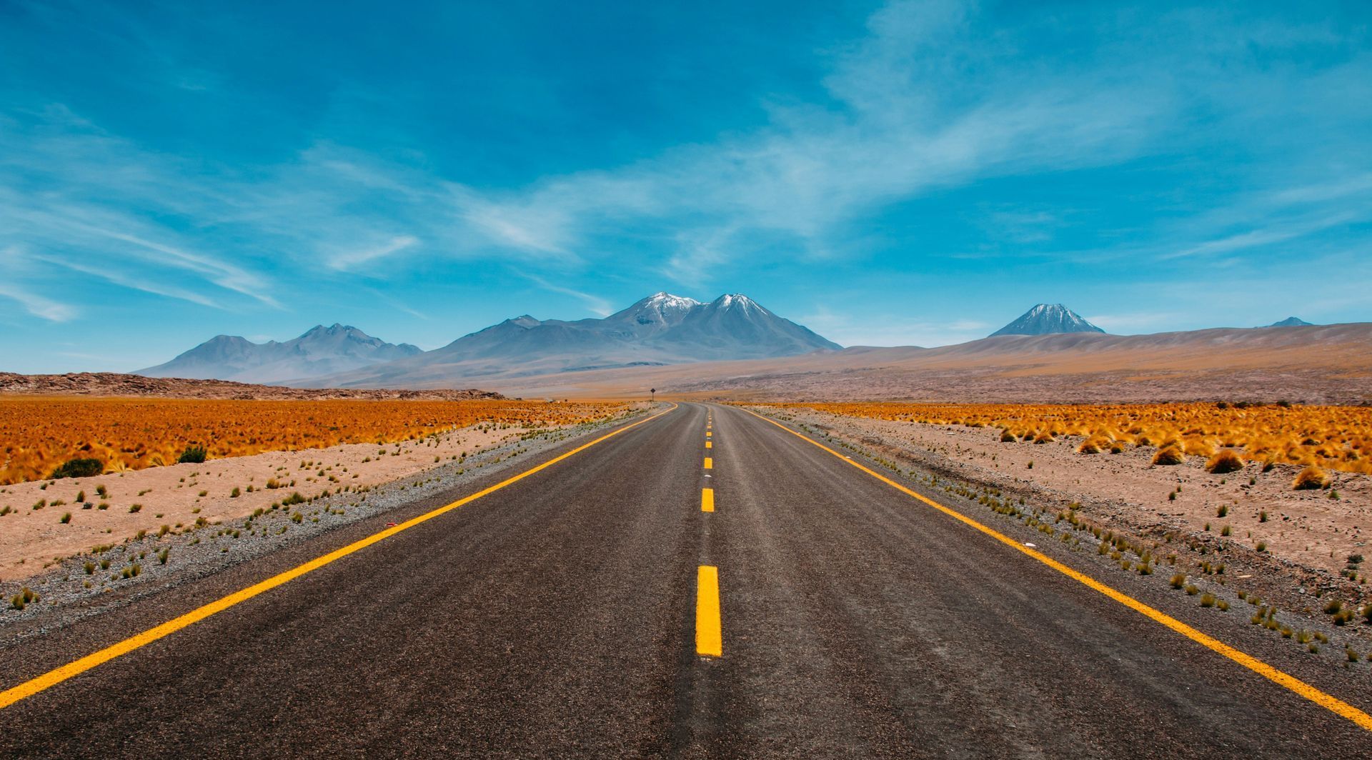 An empty road in the middle of a desert with mountains in the background.