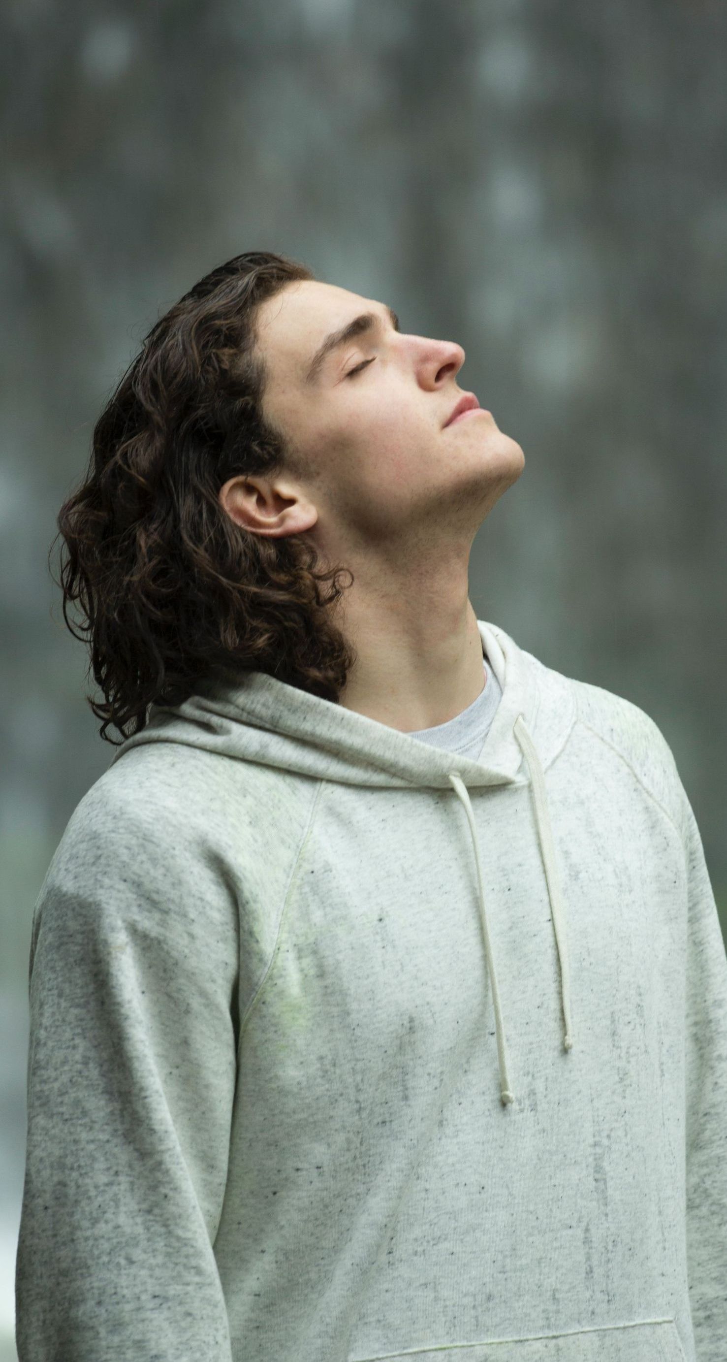 a young man with long hair is wearing a hoodie and looking up at the sky.