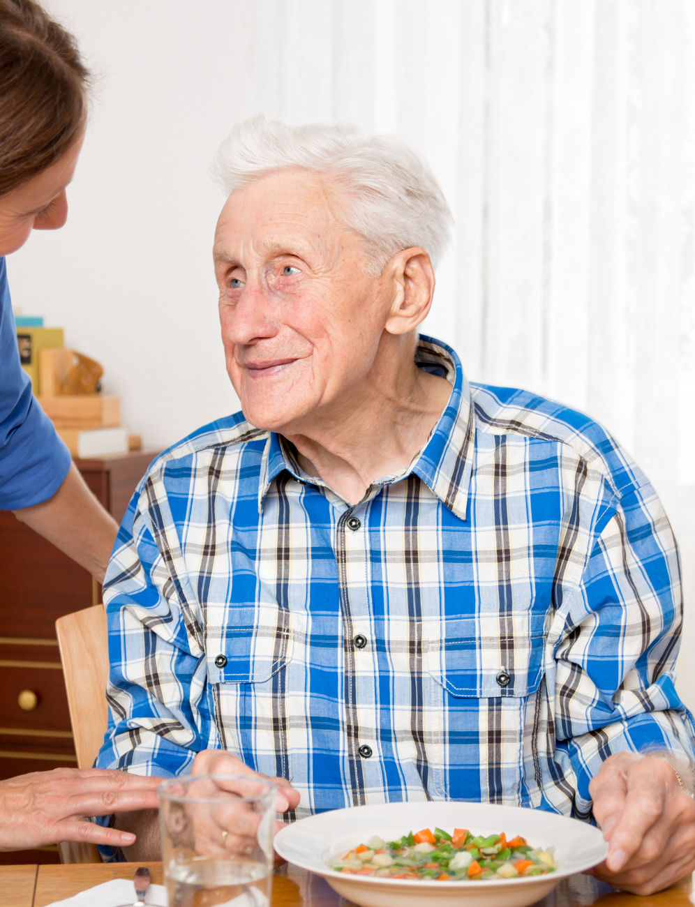 An elderly man is sitting at a table eating a bowl of soup.