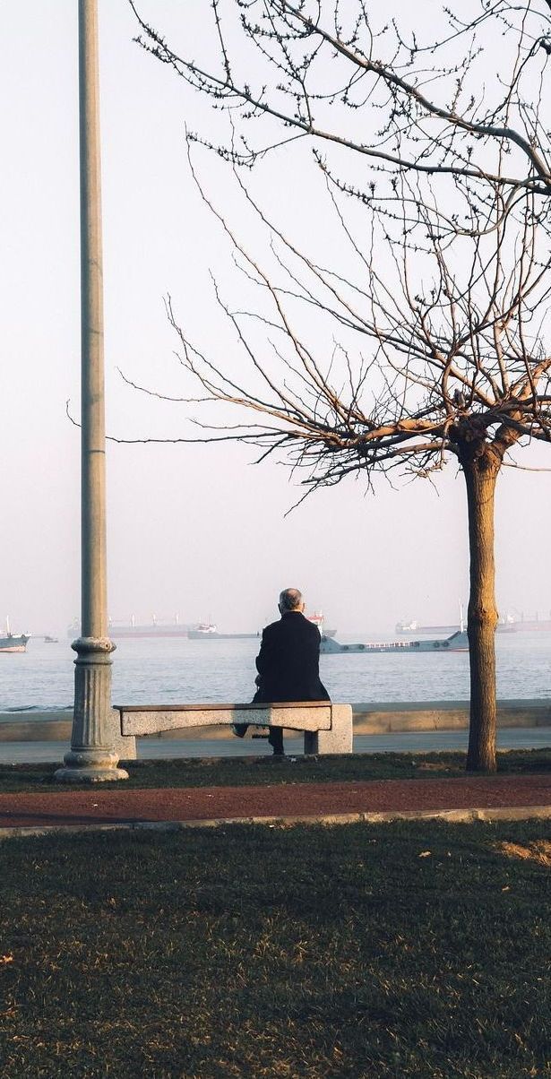 A man is sitting on a bench looking at the ocean.