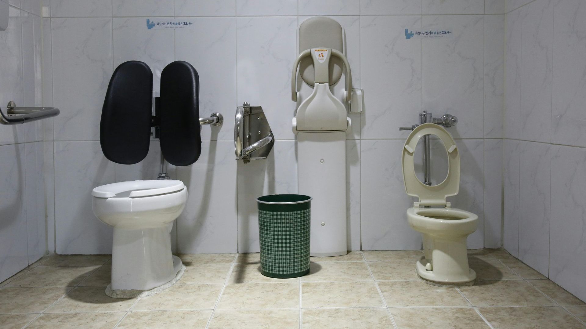 A bathroom with three toilets and a trash can