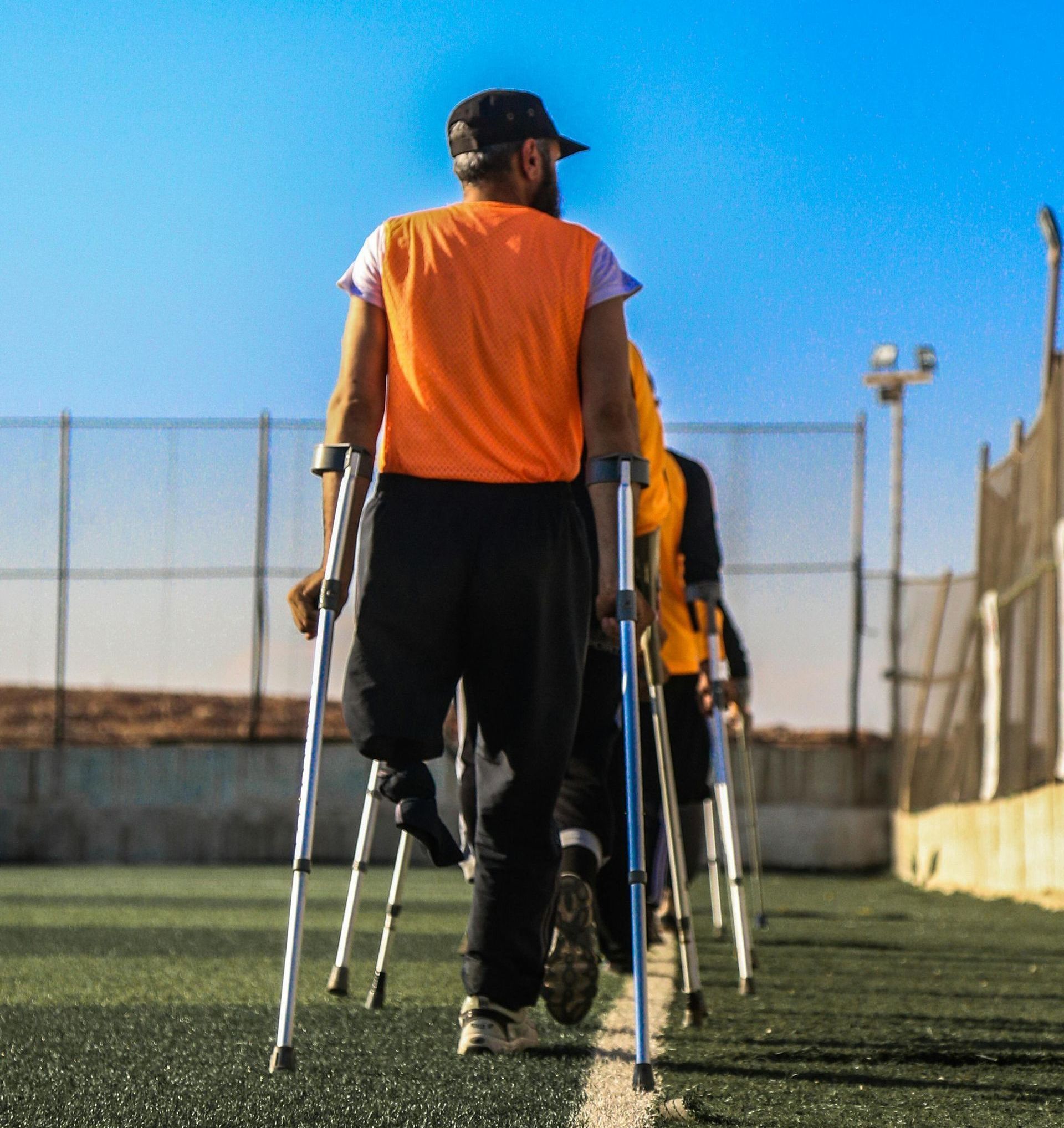 A man in an orange shirt is walking with crutches