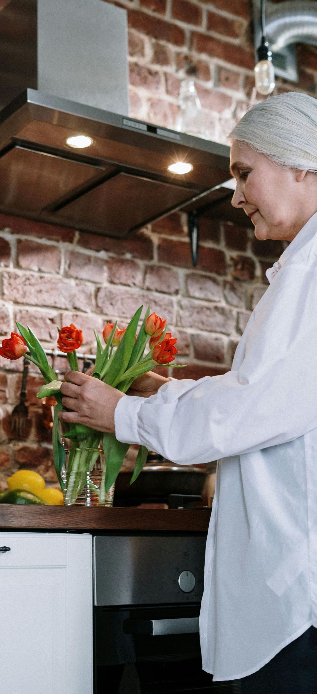 A woman is arranging flowers in a vase in a kitchen.