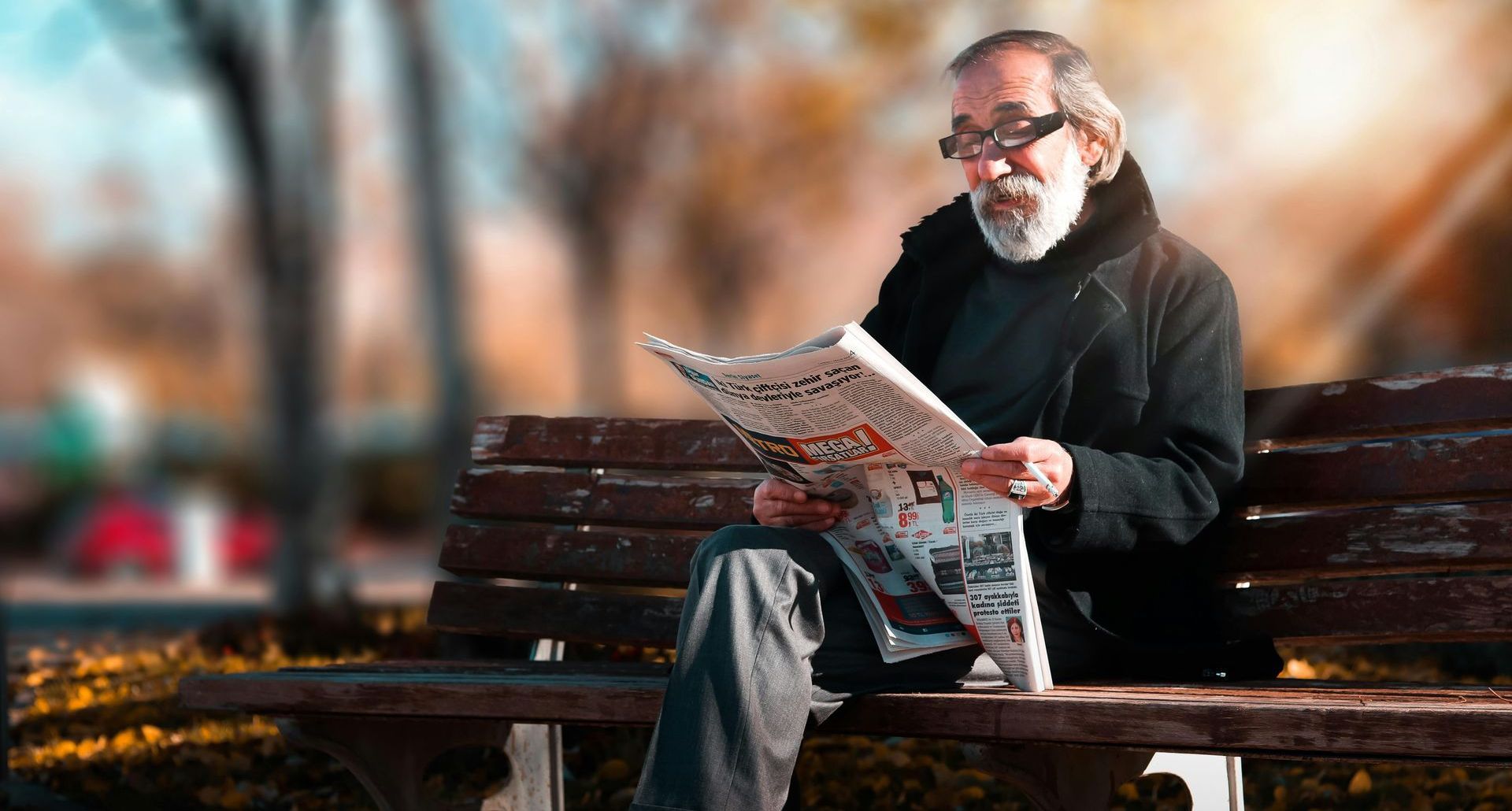 A man is sitting on a bench reading a newspaper.