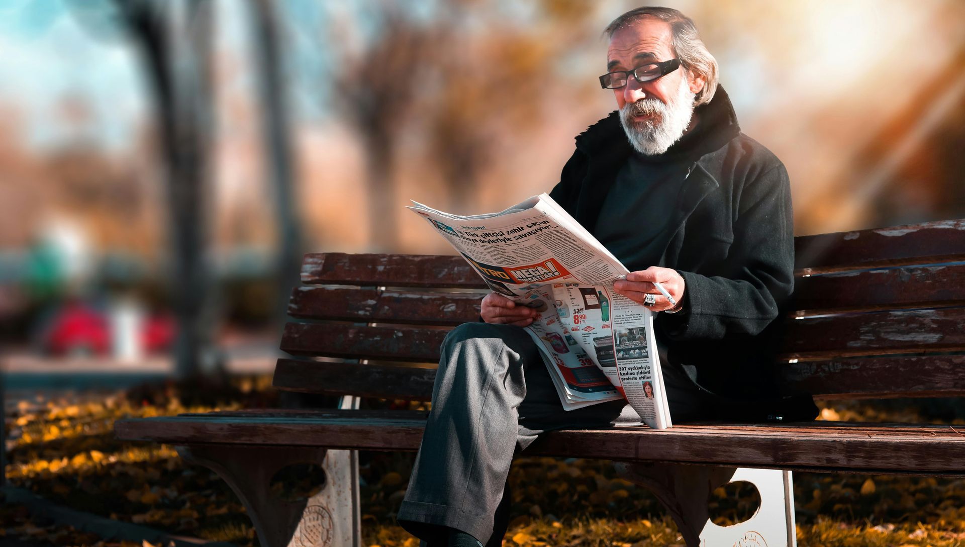 A man is sitting on a bench reading a newspaper.