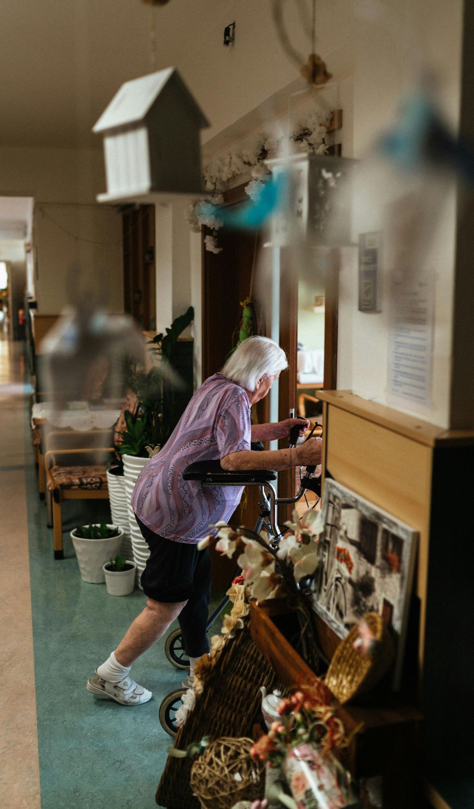 An elderly woman is pushing a walker down a hallway