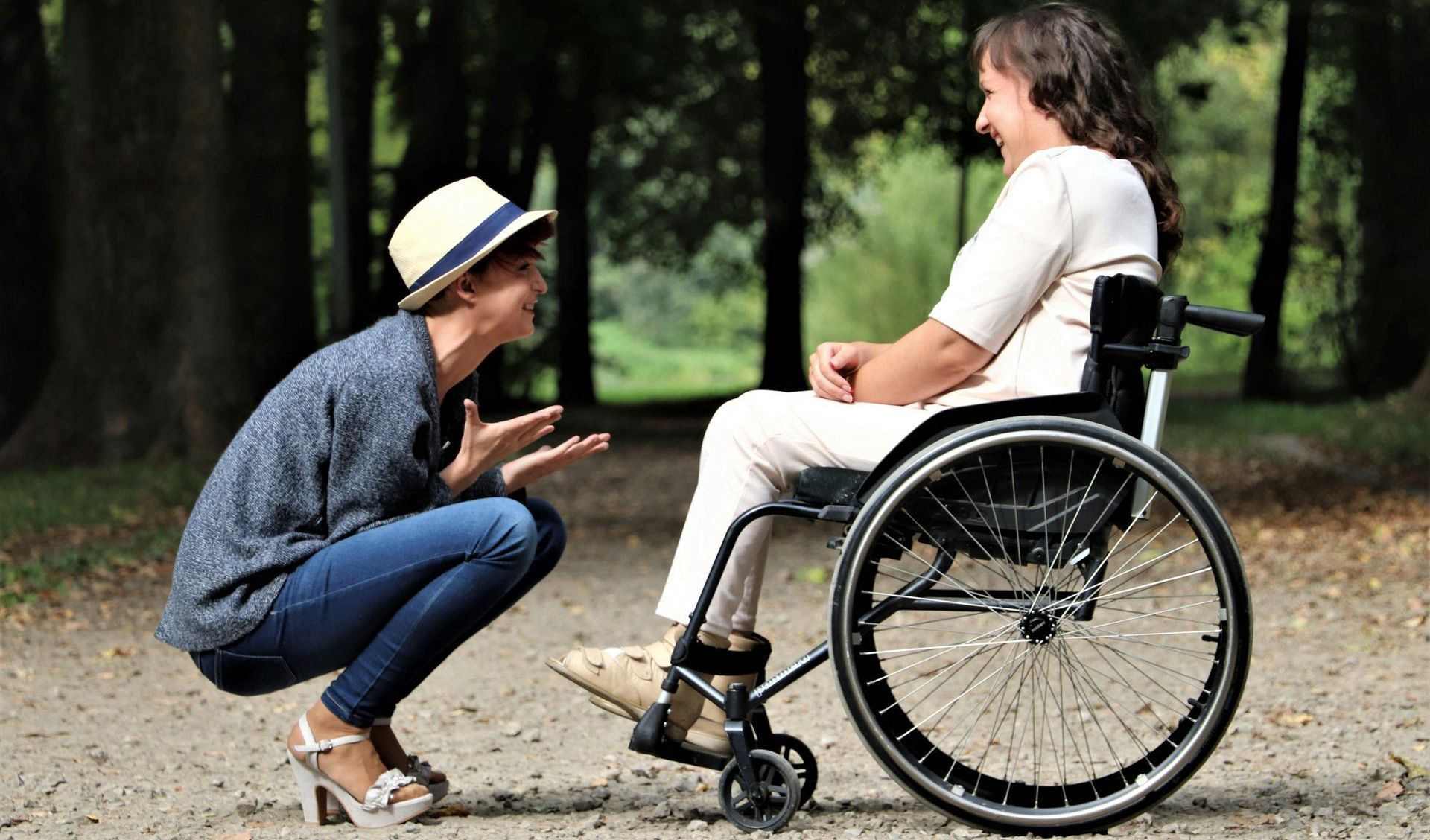 A woman is squatting down next to a woman in a wheelchair.