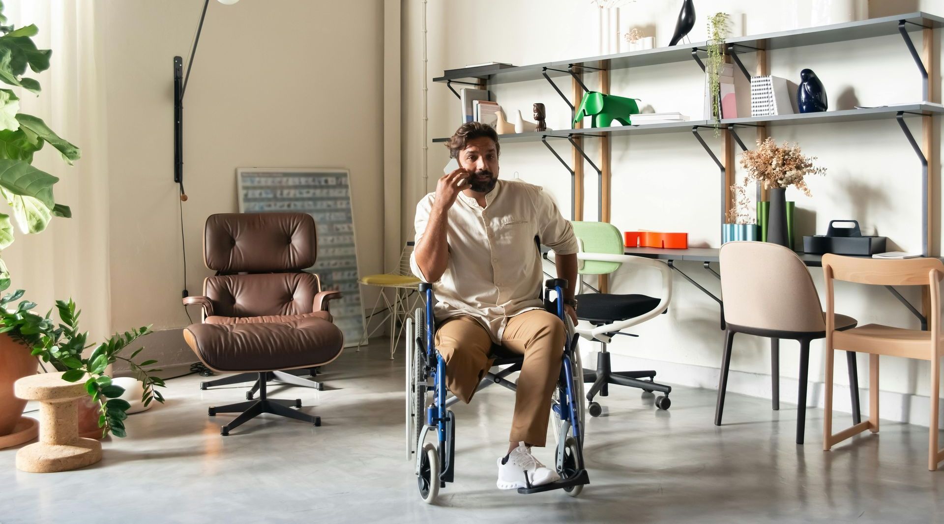 A man in a wheelchair is sitting in a living room talking on a cell phone.