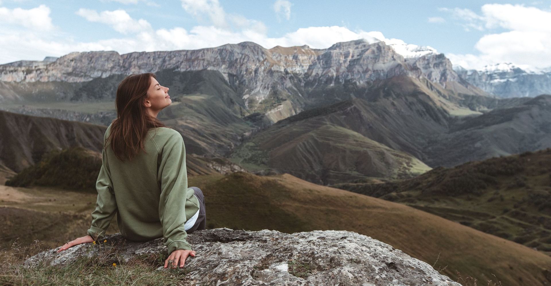 a woman is sitting on top of a mountain looking at the mountains .