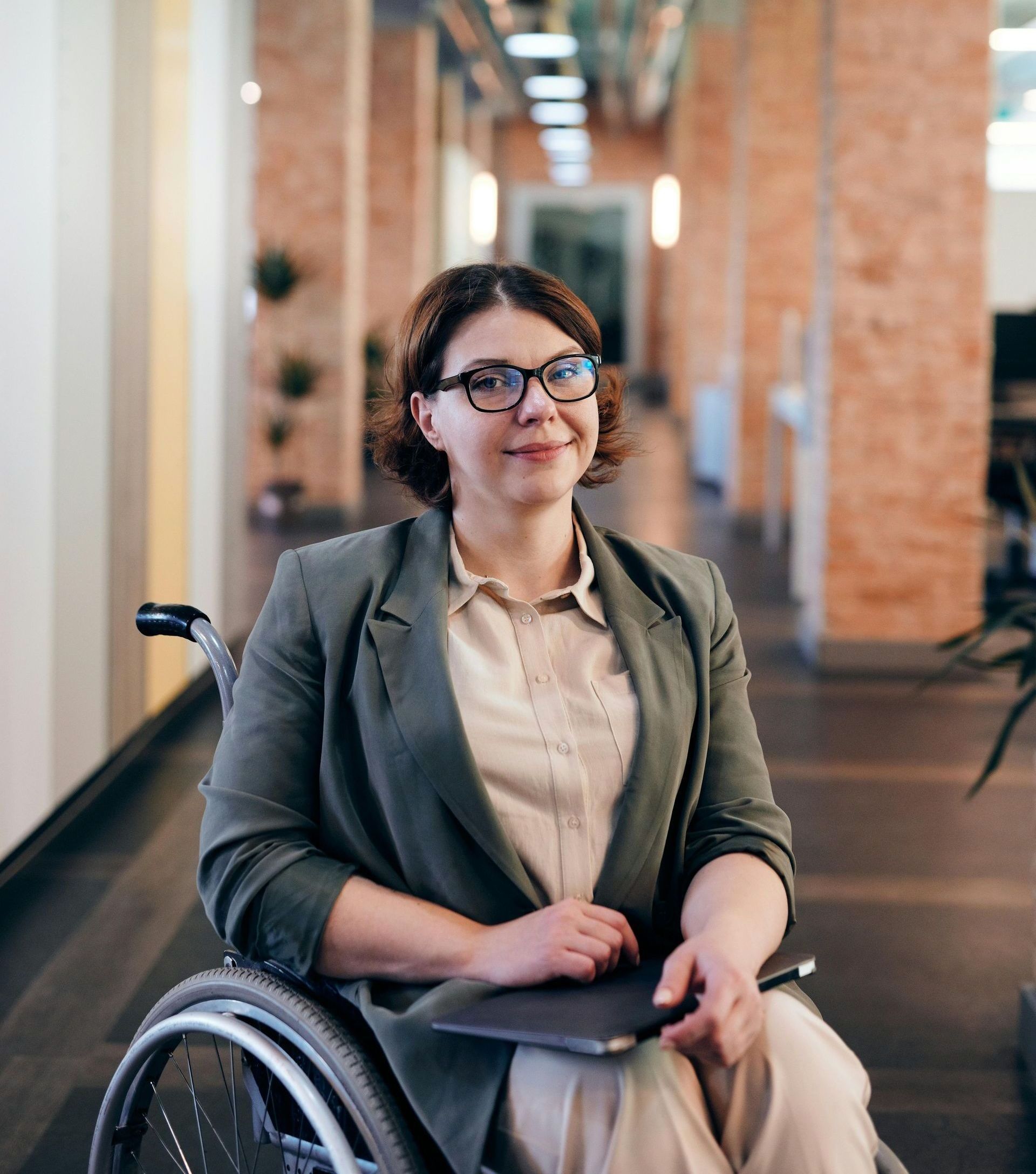 A woman is sitting in a wheelchair holding a laptop.