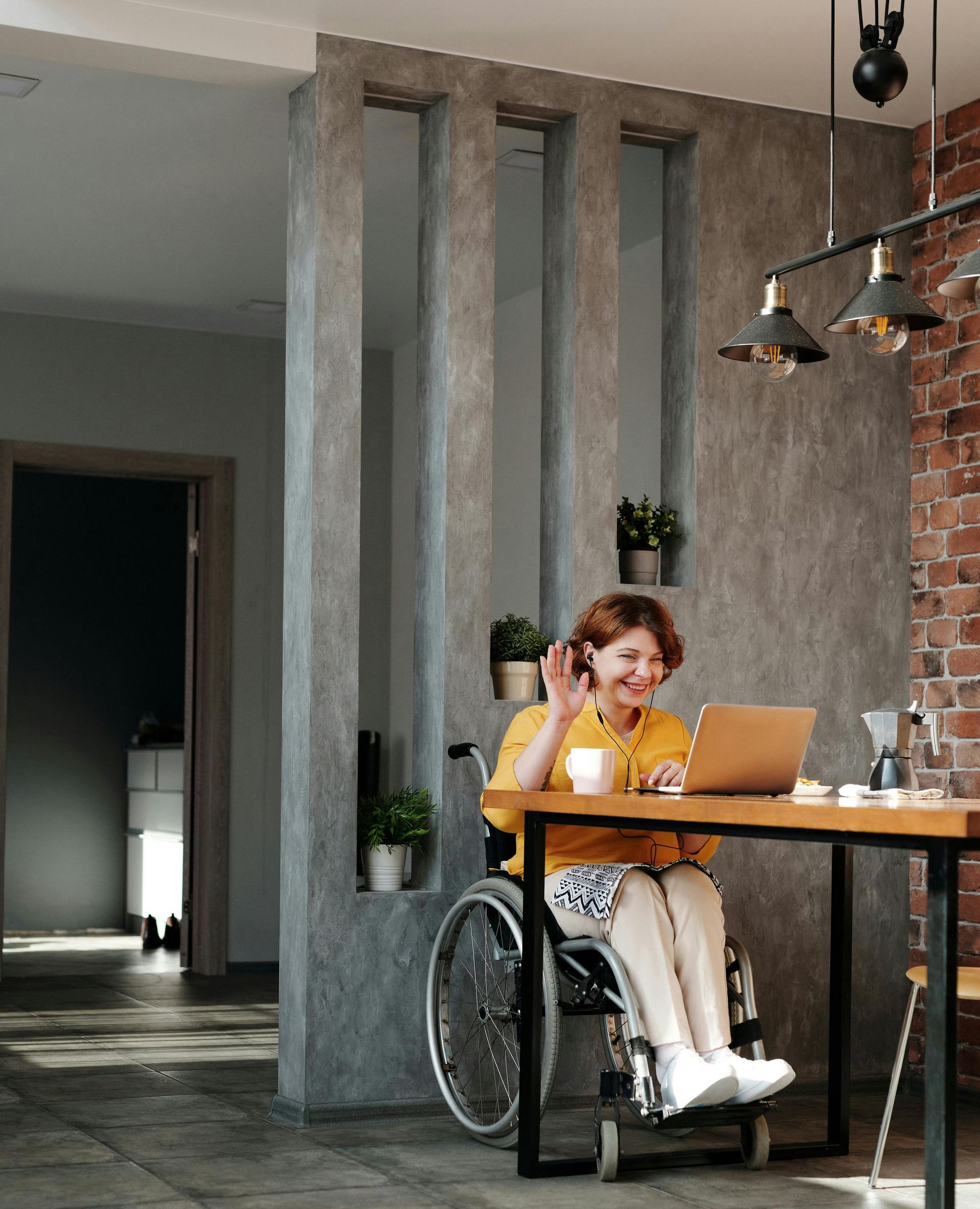 A woman in a wheelchair is sitting at a table using a laptop computer.