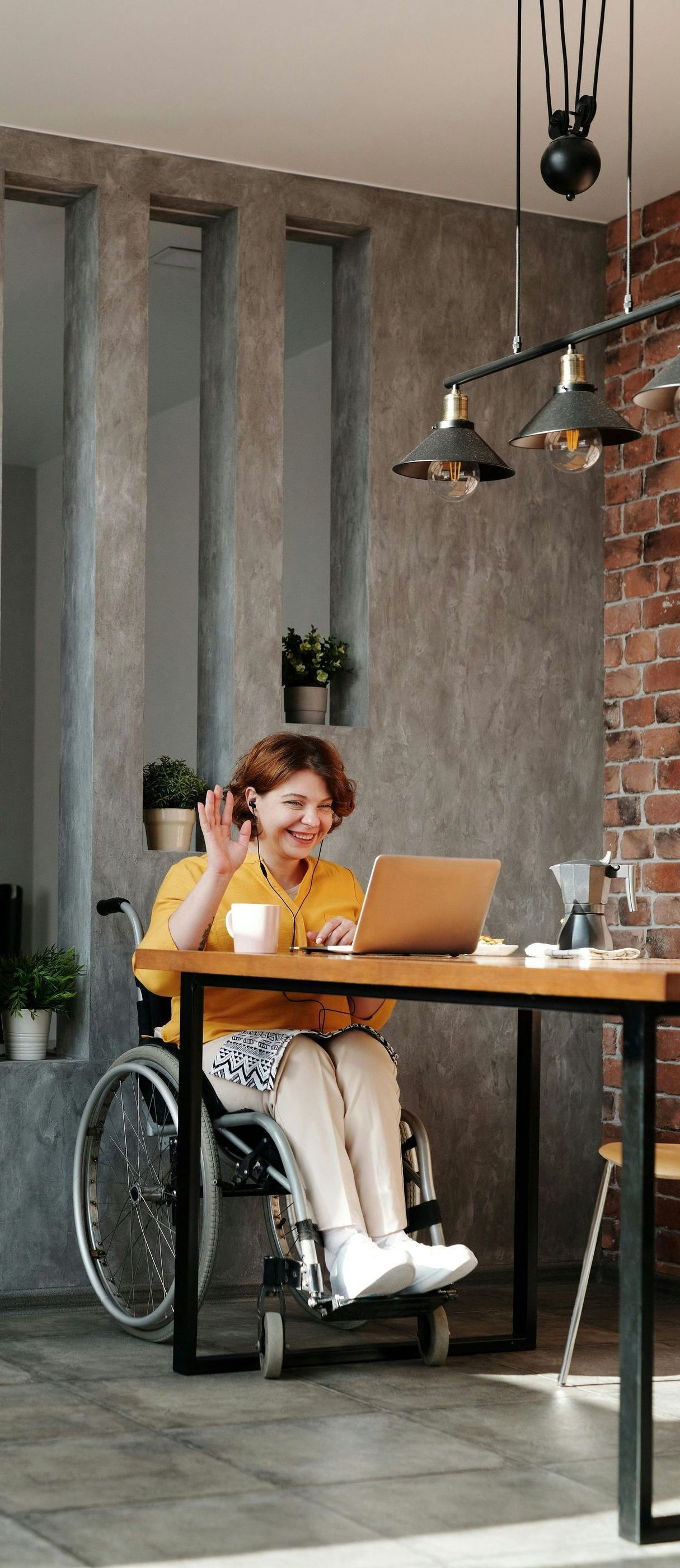 A woman in a wheelchair is sitting at a table with a laptop.