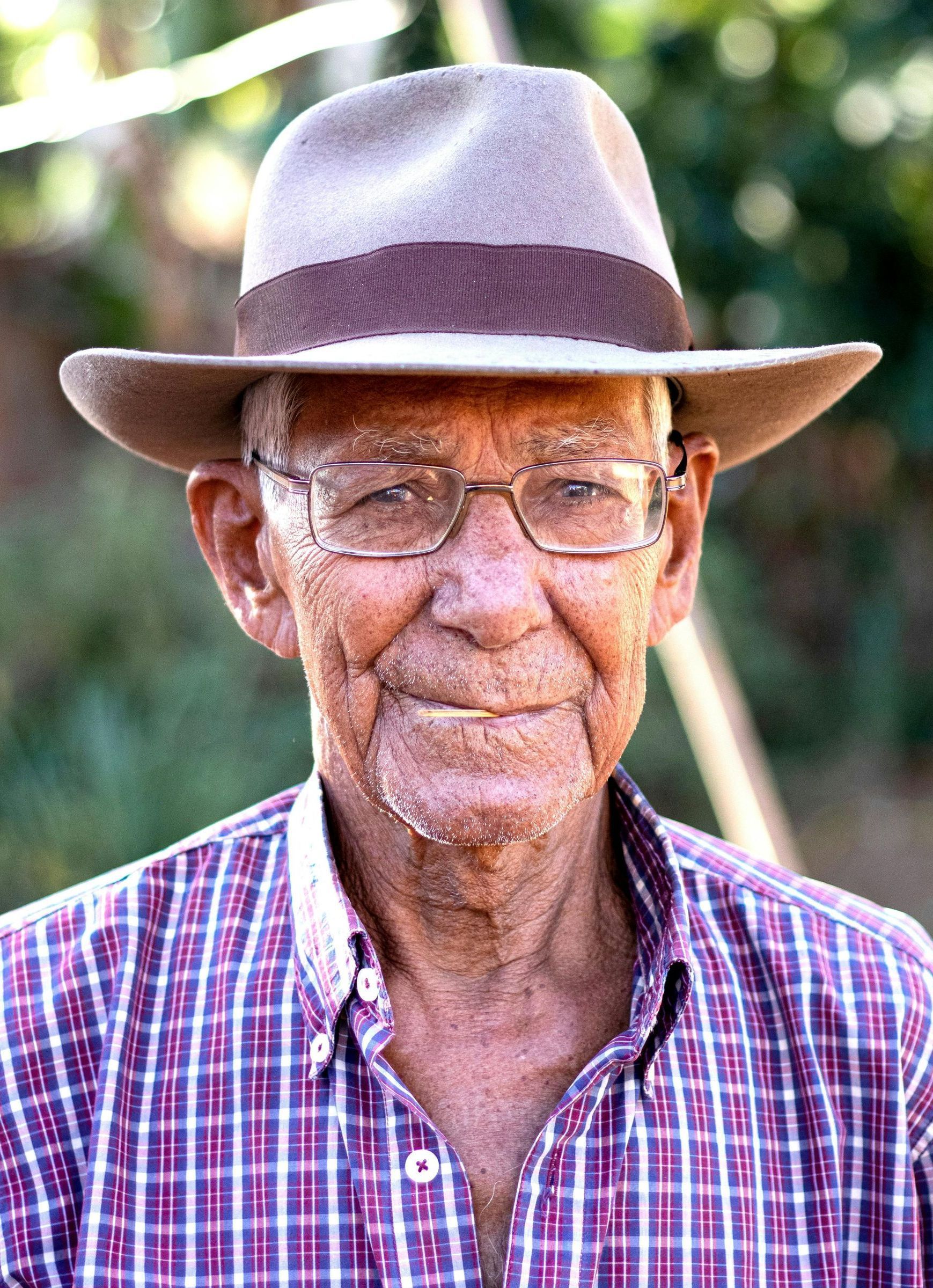 An older man wearing a hat and glasses is smiling for the camera.