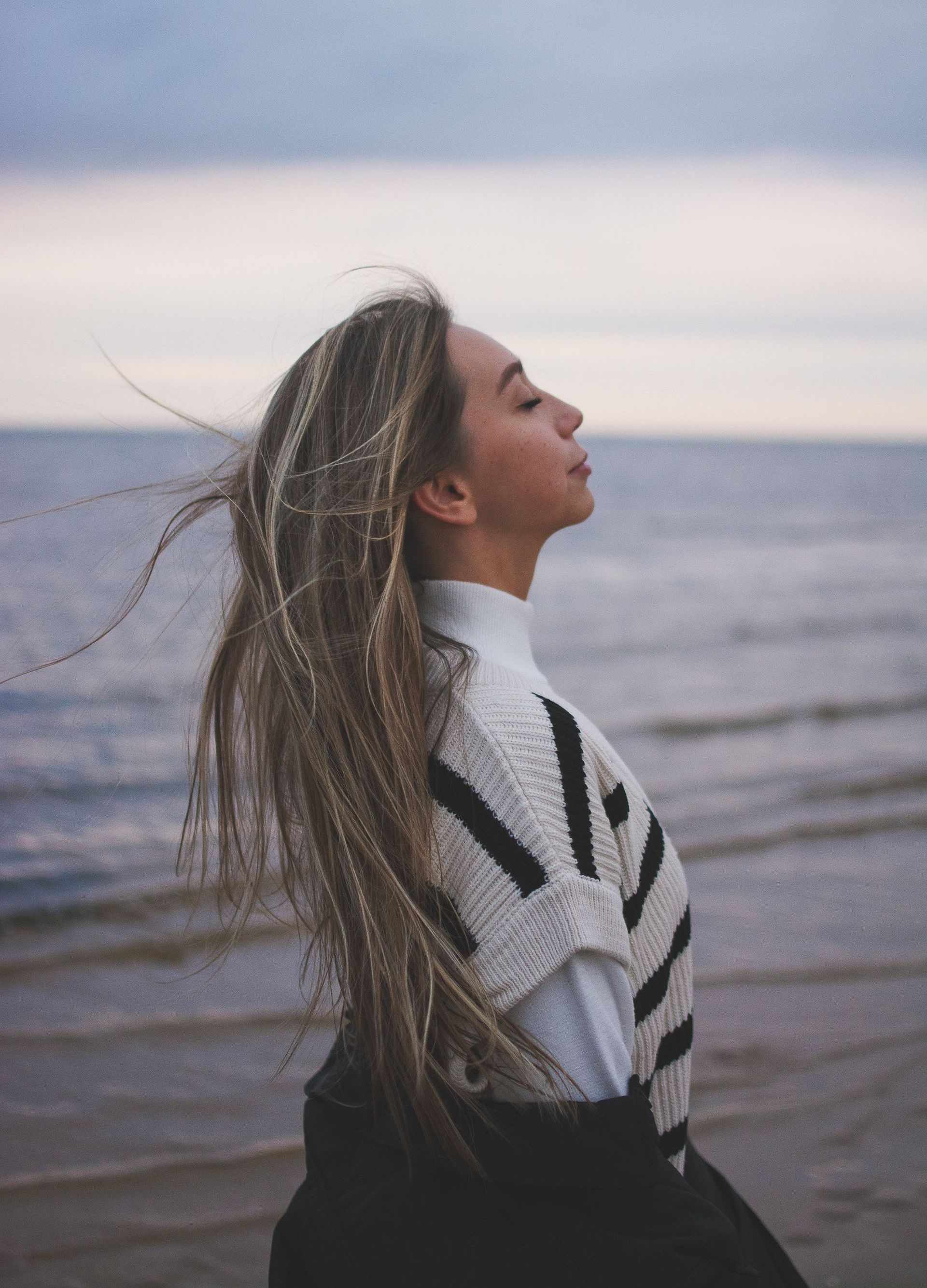 a woman is standing on a beach with her eyes closed and her hair blowing in the wind.